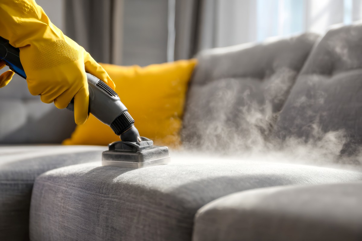 person wearing yellow gloves vaccuming a sofa